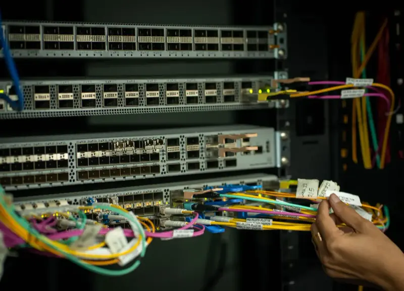 Hand managing colorful fiber cables at a switch in a server room