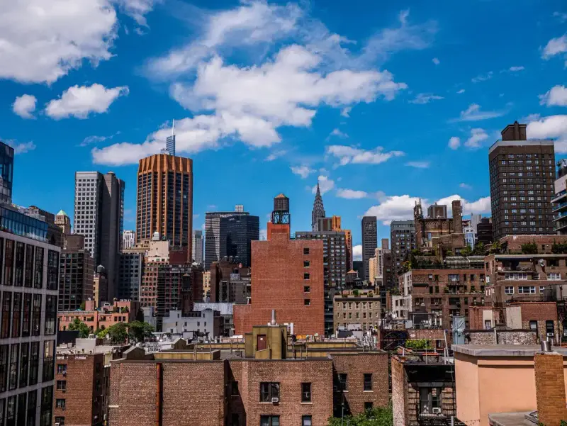 Brick rooftops and Midtown towers under a bright sky with white clouds