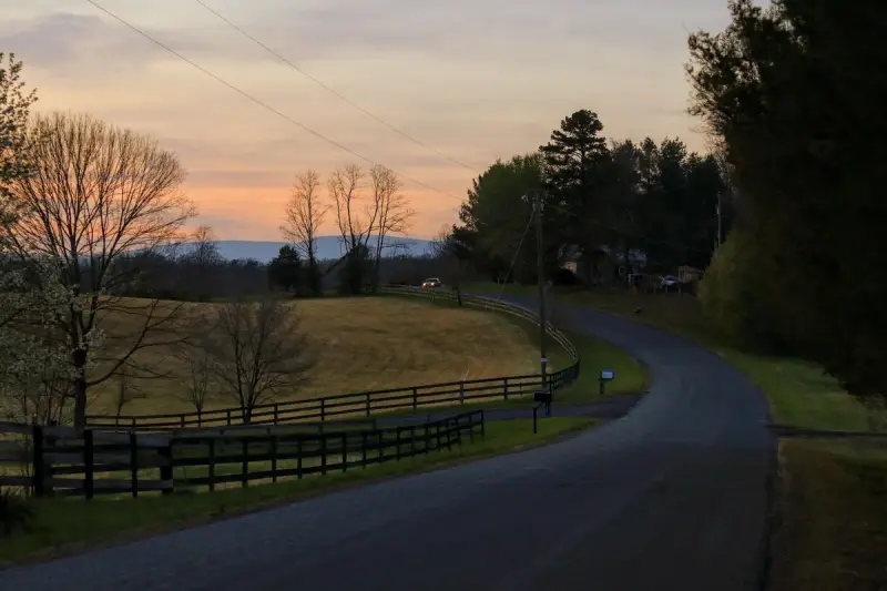 Country road with a wooden fence curving through Virginia fields at sunset