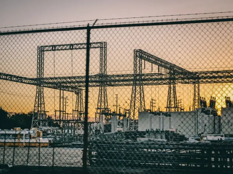 Substation gantries and transformers at sunset behind a fence