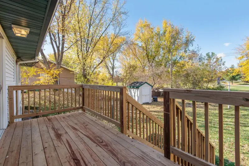 Raised wood deck with a spindle railing looking over a backyard lawn and autumn trees