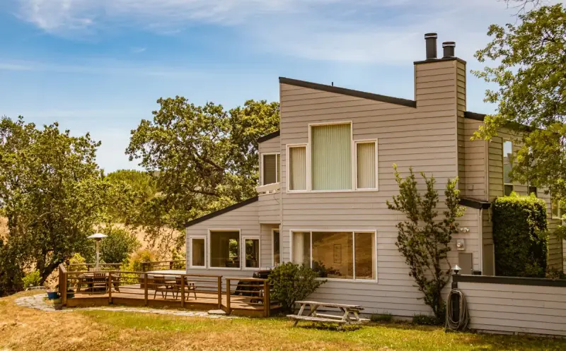 Sided house with a wood deck and railing on the lawn under oak trees