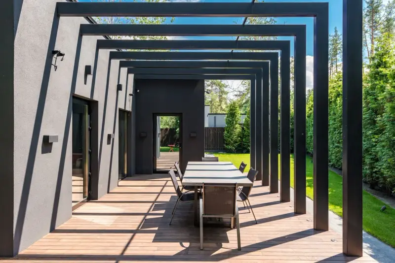 Dining table on a hardwood deck framed by a run of dark steel pergola beams