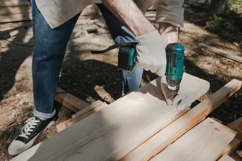 Gloved hands drilling into a pine board with a cordless drill
