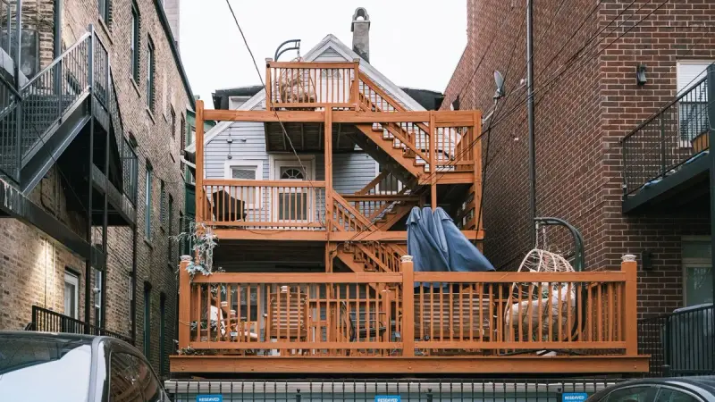 Multi-level stained wood deck with stairs and railings behind a house between brick buildings