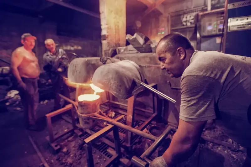 Metalworkers in protective gear tending a glowing industrial furnace