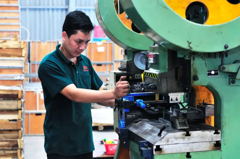 Operator in a green polo running a punch press stamping metal parts