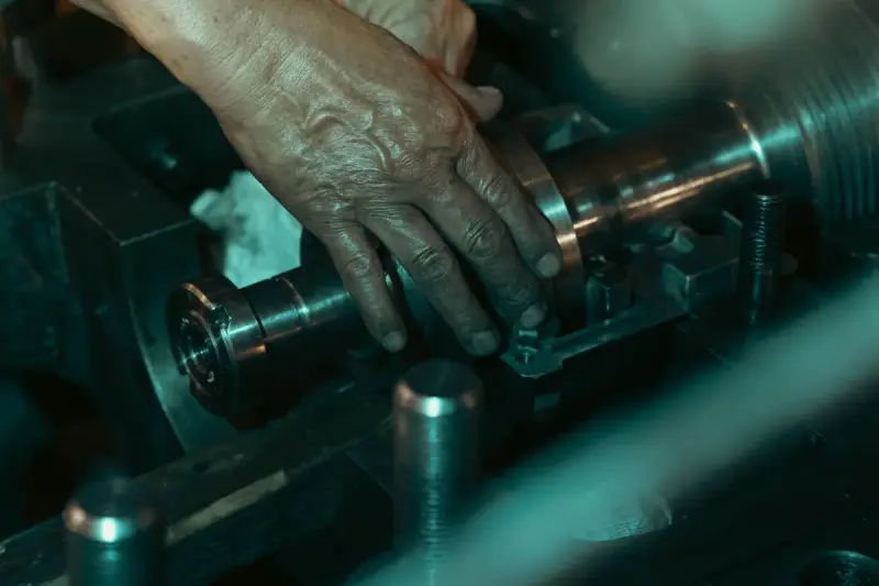 Hand adjusting a polished steel part clamped in a lathe chuck under teal light
