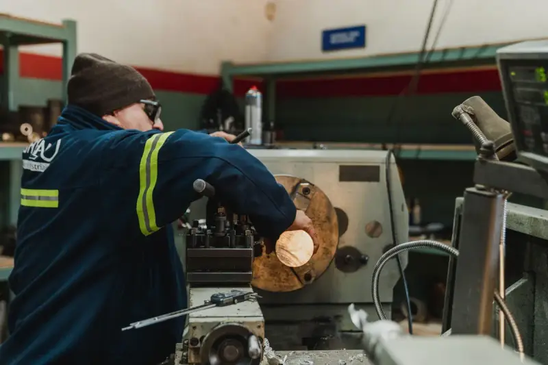 Worker operating a large metal lathe in a busy machine workshop