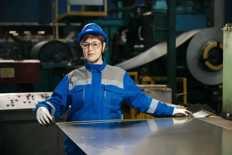 Woman in protective gear handling a steel sheet in a factory