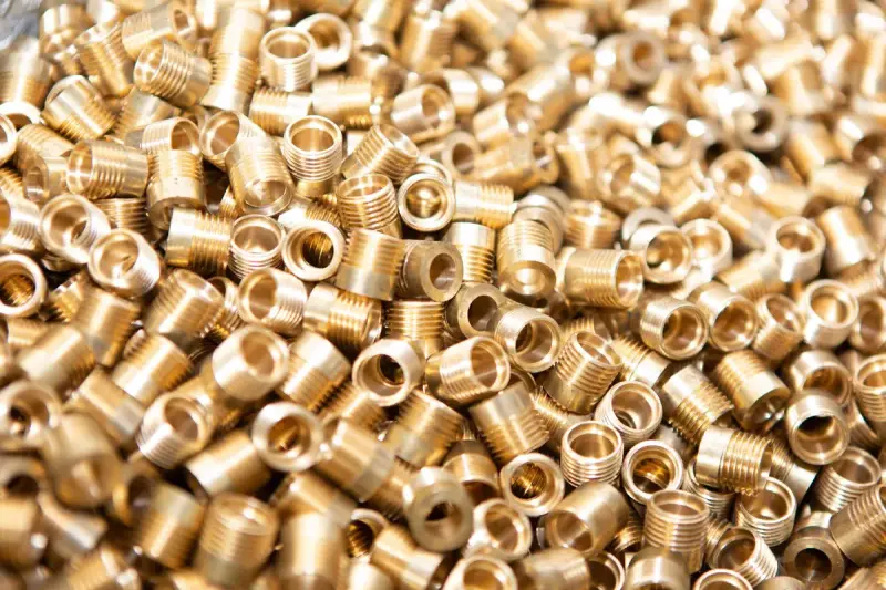 Pile of freshly machined brass threaded inserts glowing gold