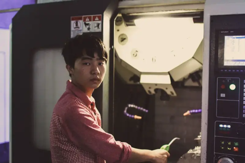 Young technician in a checked shirt working at an open CNC machining center