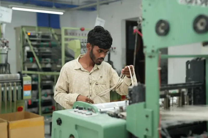 Worker in a light shirt setting up a green industrial machine in a bright factory