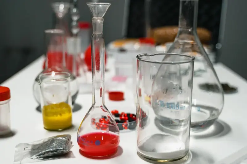 Volumetric flasks, beakers and dishes of red and yellow compounds on a white lab table