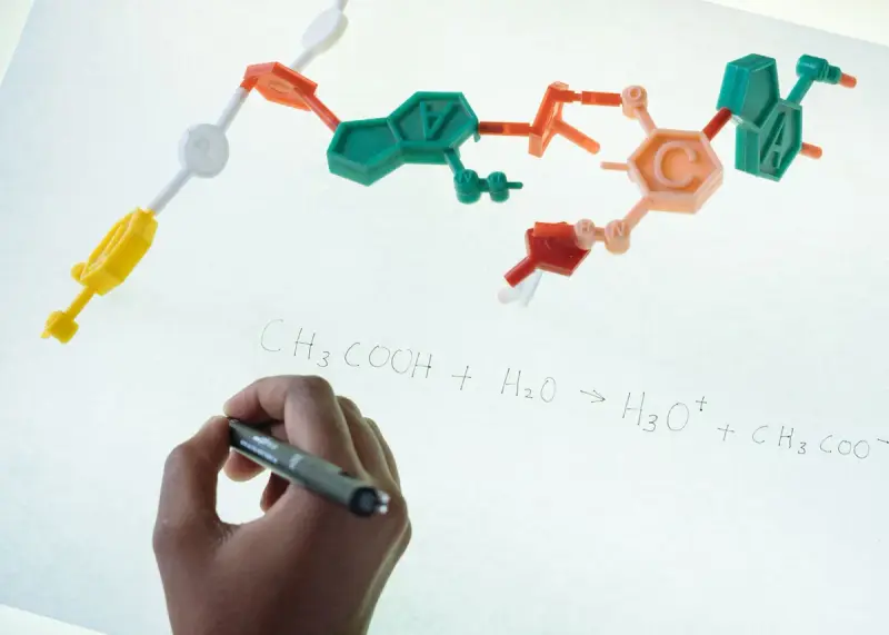 Colorful ball-and-stick molecule model on glass with a hand writing a reaction equation