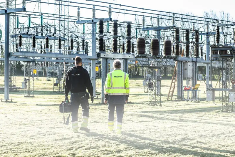Two workers inspecting equipment at an outdoor electrical substation