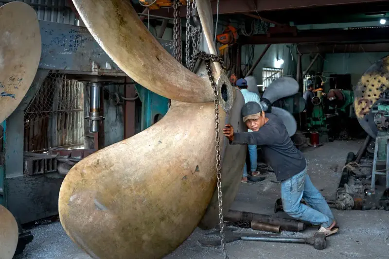 Worker positioning a huge bronze ship propeller in a heavy machining workshop