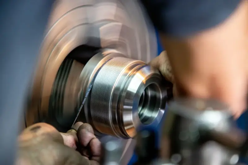 Hands finishing a threaded metal part as it spins on a lathe