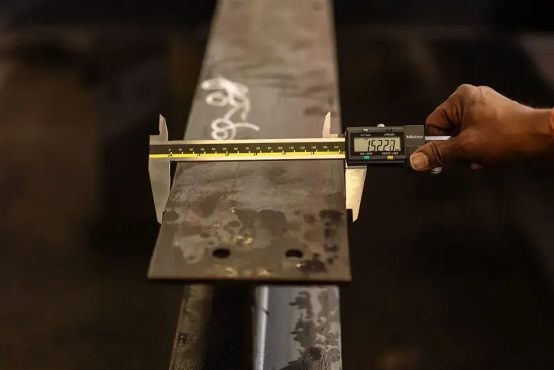 Hand holding a digital caliper across the width of a steel bar