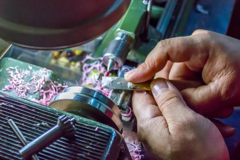 Hands guiding a cutting tool on a metal lathe with curled chips piling up