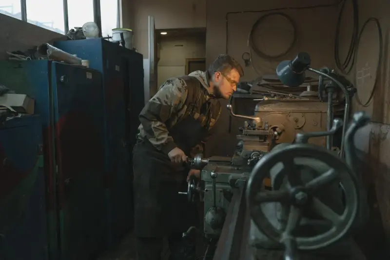 Machinist in safety glasses turning a part on a manual lathe in a workshop