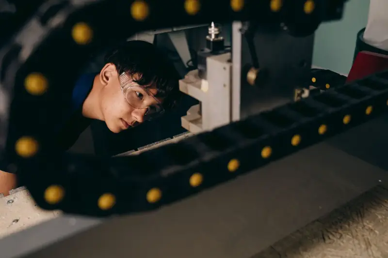 Young engineer in safety glasses inspecting a machine through its cable carrier chain