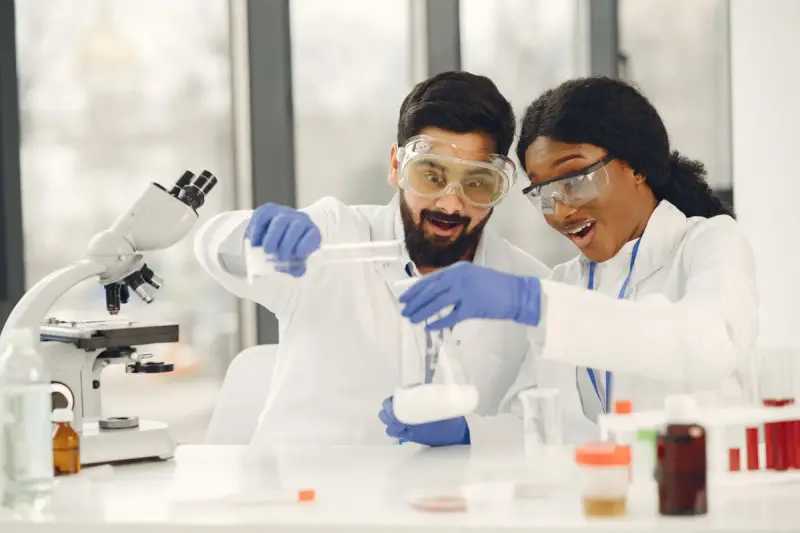 Two scientists in safety glasses reacting to a result at their lab bench