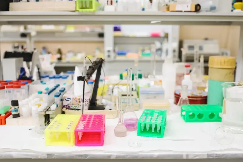 Busy laboratory bench with colored tube racks, flasks and reagent bottles