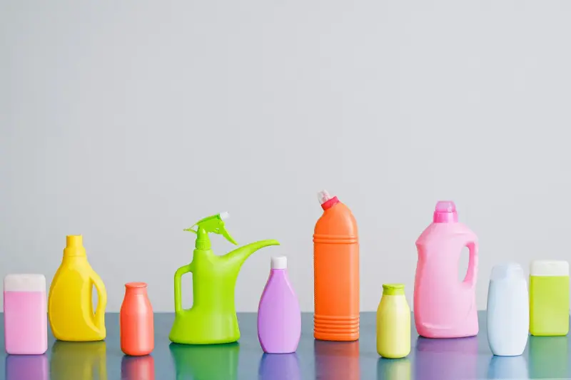 Row of colorful unlabeled household cleaning bottles against a white wall