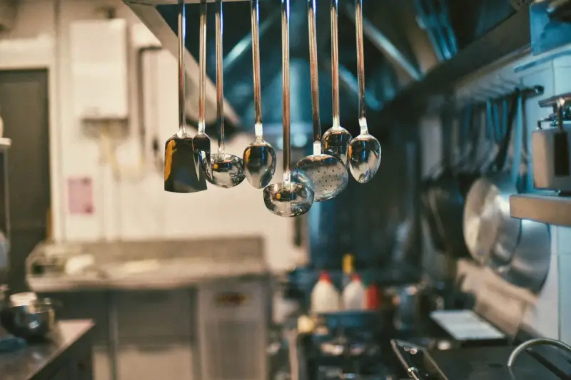 Stainless steel ladles and kitchen utensils hanging on a rail in a kitchen