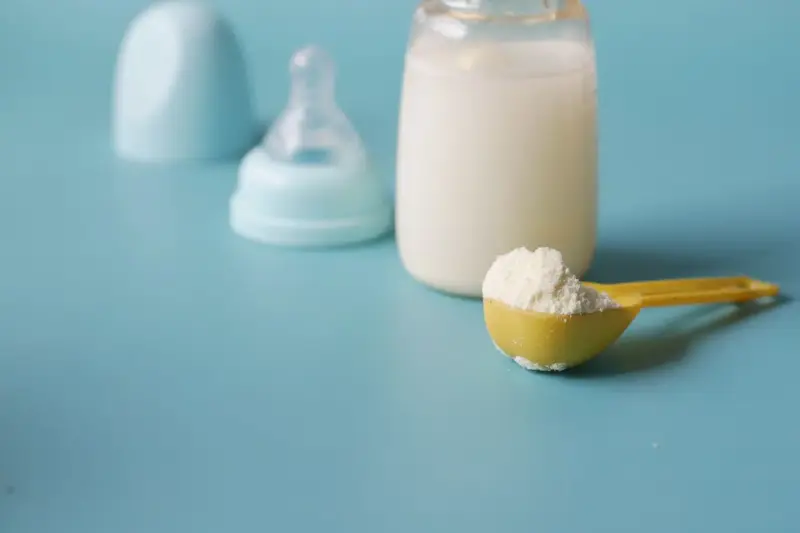 Scoop of baby formula powder beside a baby bottle on a blue background