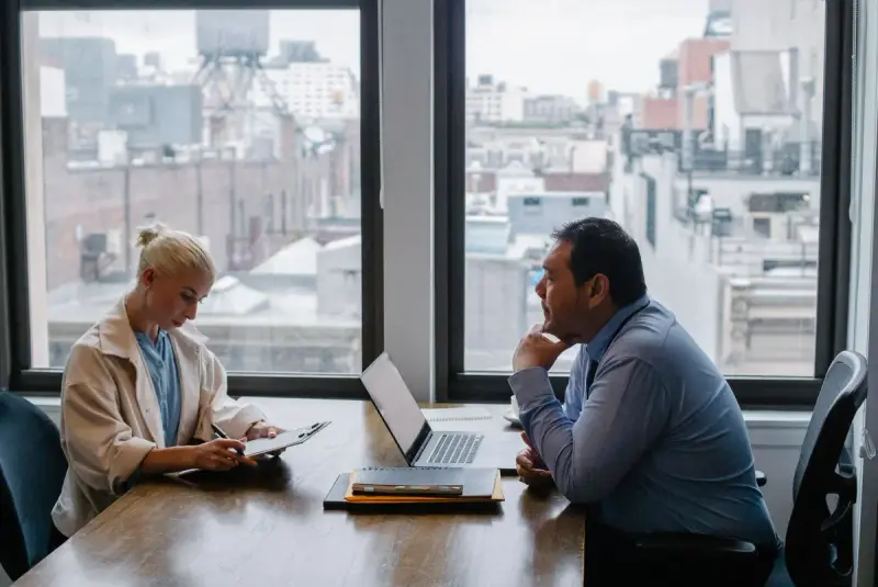 Businessman and businesswoman meeting at a table by a window with a city view