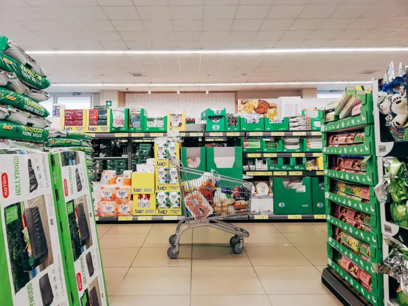Shopping cart in a bright grocery aisle with green shelving and stocked displays