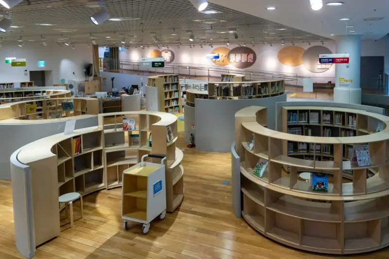 Library floor with curved wooden shelving rings and reading nooks under a grid ceiling