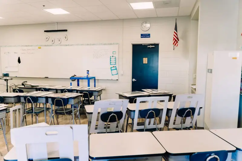Empty classroom with white desks, a whiteboard wall and an American flag by the door
