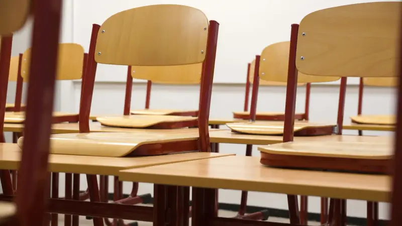 Close view of beech-veneer school chairs with burgundy frames stacked on desks