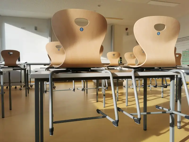 Molded plywood classroom chairs flipped onto desks in a tidy room