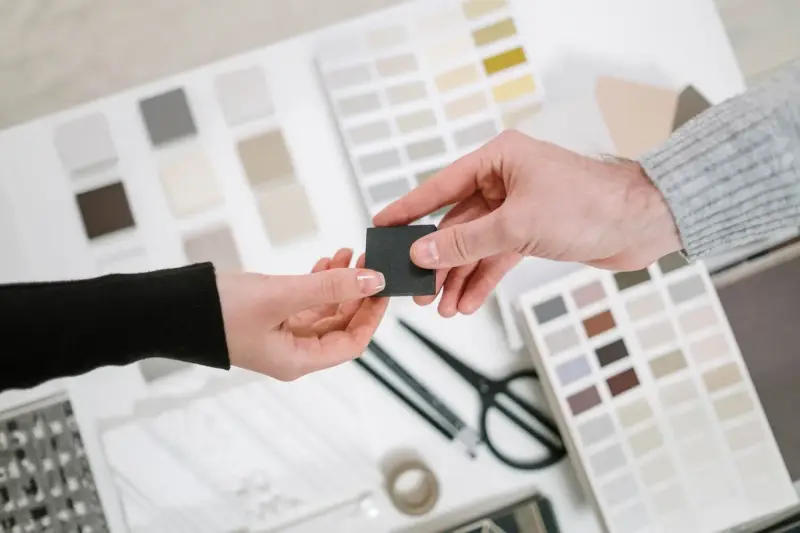 Two hands passing a dark finish chip over fanned paint and laminate sample cards