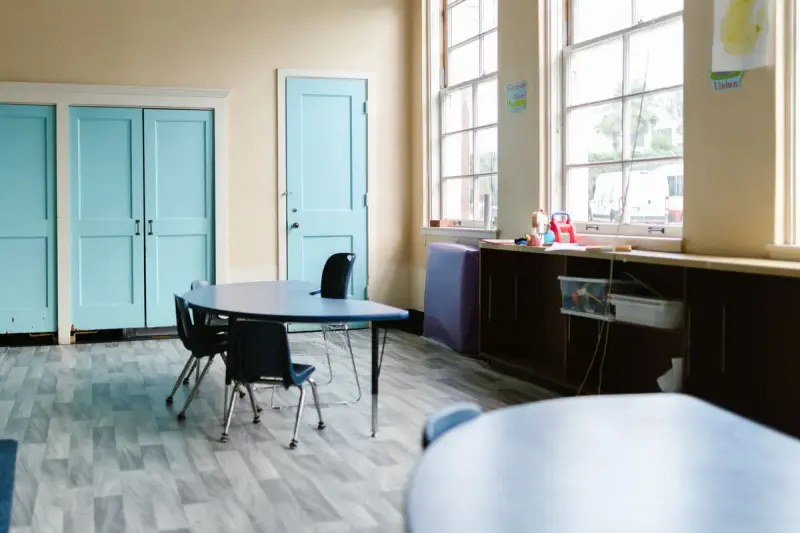 Empty classroom with a kidney-shaped table, small chairs and teal doors in warm daylight