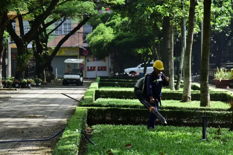 Grounds worker in a hard hat using a backpack leaf blower along park hedges