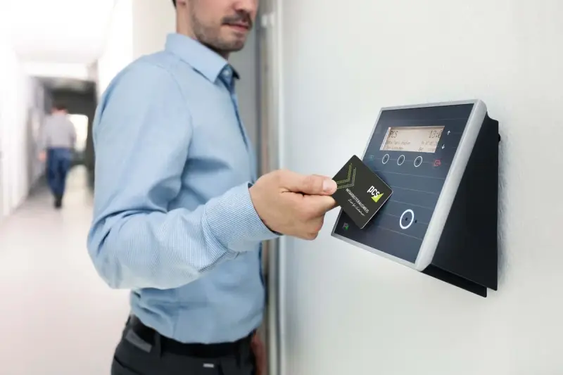 Hand holding an access card over a wall-mounted RFID card reader