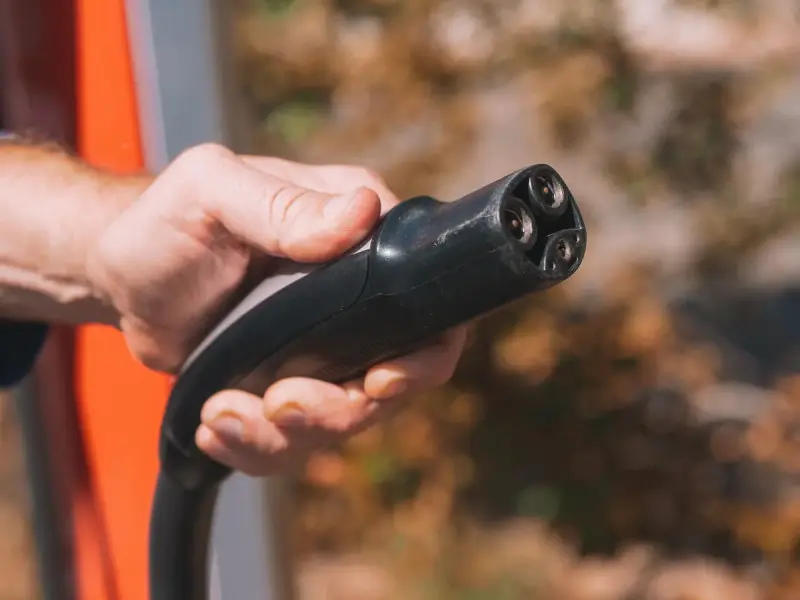 Hand holding an EV charging plug at an outdoor station