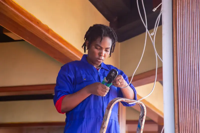 Female electrician on a ladder holding cables during an indoor installation