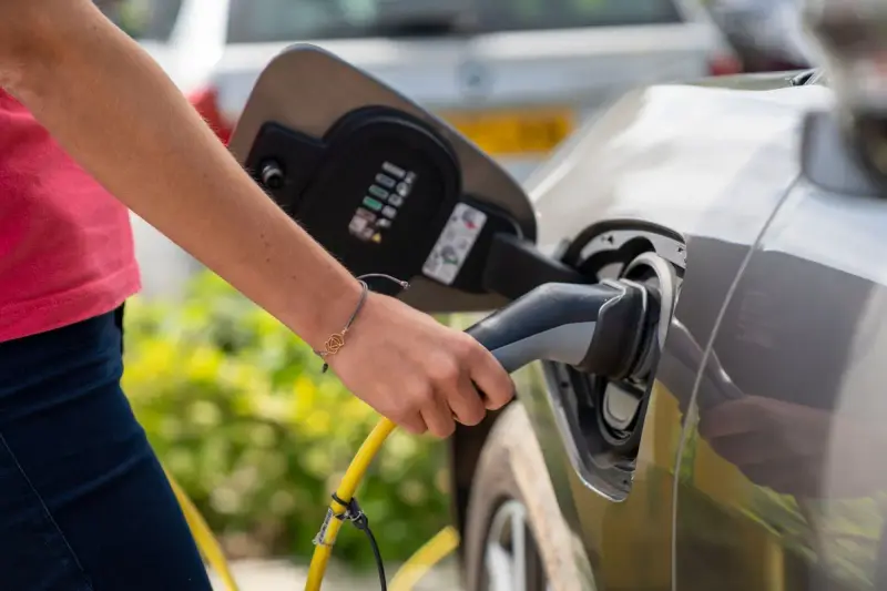 Person plugging a charging cable into an electric car at an outdoor station