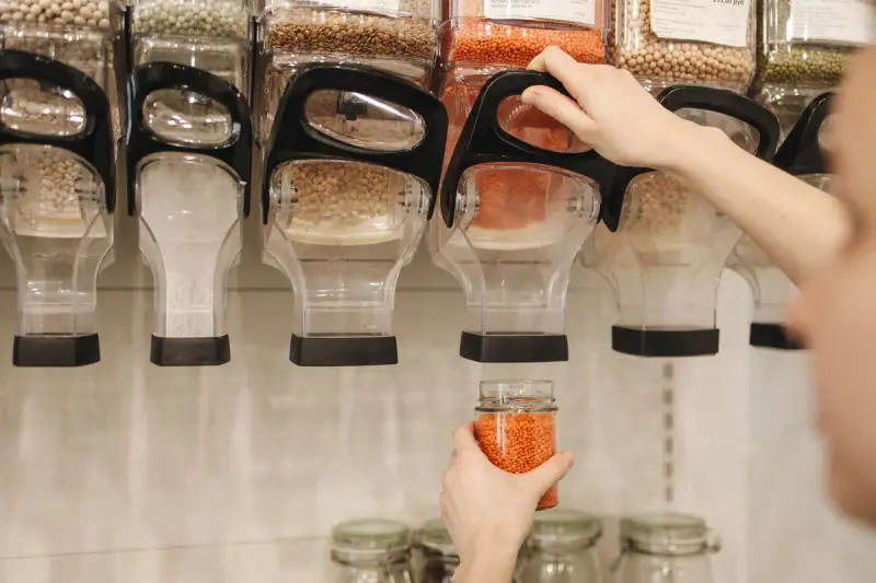 Shopper filling a glass jar with red lentils from a row of bulk food dispensers