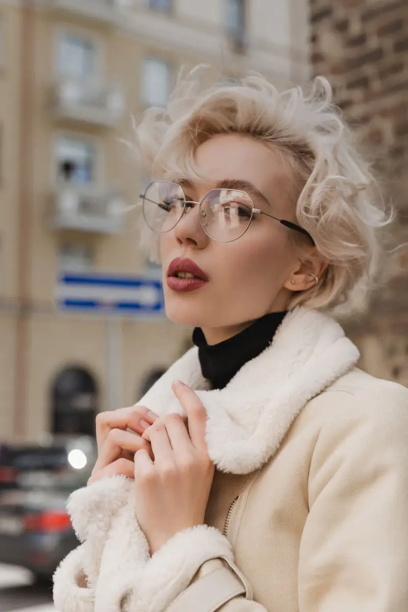 Blonde woman in thin clear-rim eyeglasses and a cream shearling coat on a city street