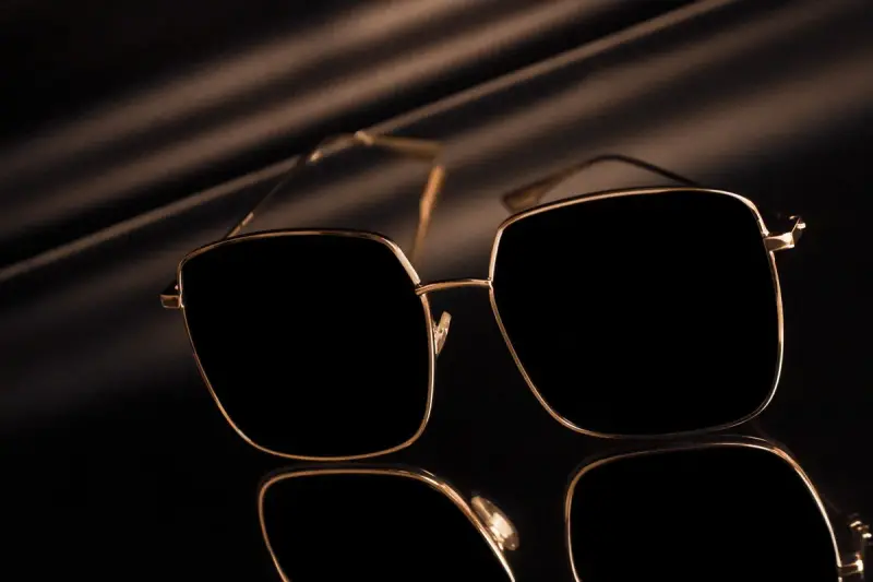Square gold-framed sunglasses reflected on a glossy surface