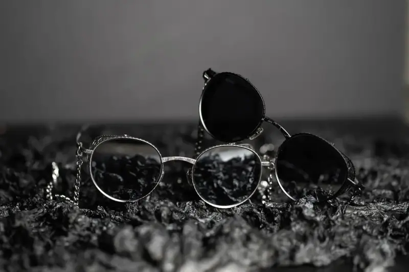 Three metal sunglasses with chains on a dark textured surface, in black and white
