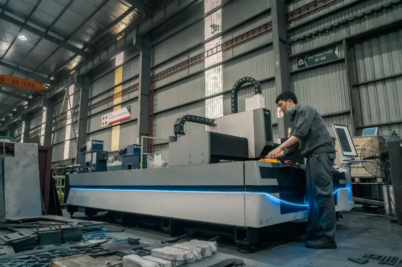 Operator at the controls of a large fiber laser cutting table in a high-bay fabrication plant