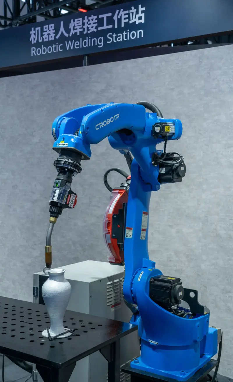 Robotic welding station with a robot arm welding a metal part